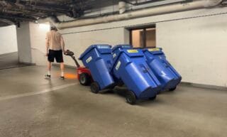 Version 4 cabas du porte-cabas Bin Butler 16 Voici un opérateur utilisant le déménageur de bennes à ordures V-move XL+ avec le transporteur de bacs Bin Butler et quatre bacs de recyclage de 95 gallons.